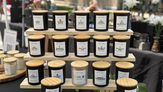 Tiered wooden display shelf holding rows of Sweet U Candles soy candles in black jars, showing how a collection of candles is organized and stored