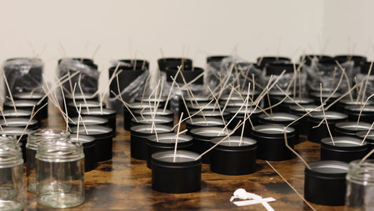 Rows of handmade candles in black tins with raw wicks on a workshop table — the candle making process at Sweet U Candles