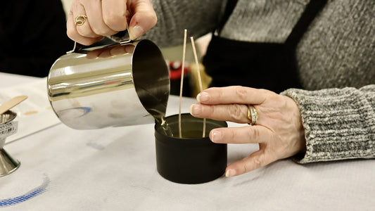 Hands pouring melted soy wax into a candle tin with two centered wicks