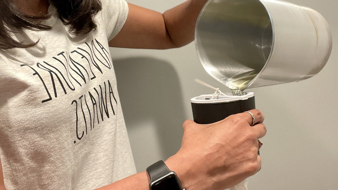 Pouring melted soy wax into a black candle jar with a wick centered in place