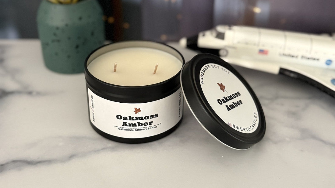 Sweet U Candles Oakmoss Amber soy candle in a black tin with the lid beside it on a marble counter