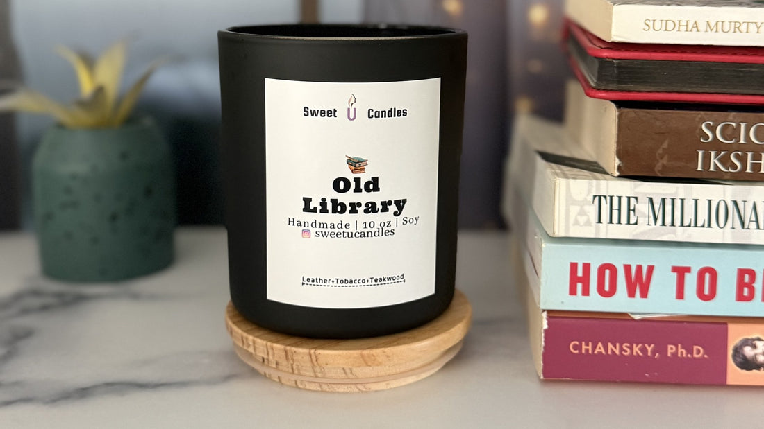 Sweet U Candles Old Library soy candle in a matte black 10 oz vessel on a marble counter with stacked books and a small plant