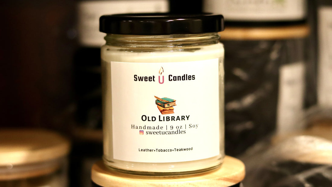 Sweet U Candles Old Library soy candle on a wooden lid in a warm, dimly lit shelf setting, a cozy fall evening mood